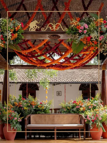 The main seating area for the Mehendi, featuring a traditional bench set against a backdrop of marigold webs and lush, wild garden-style florals. The elephant motifs add a touch of Indian heritage.