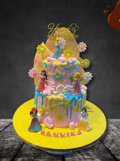 A dreamy two-tier cake featuring several Disney princesses. The pastel colors, star decorations, and drip effect create a magical backdrop for figures of Cinderella, Ariel, and others.