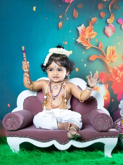 A happy little Krishna sitting on his throne, holding his flute.