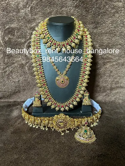 A classic mango mala set with red and green kemp stones. This rental includes a choker, long necklace, and a goddess motif vaddanam.