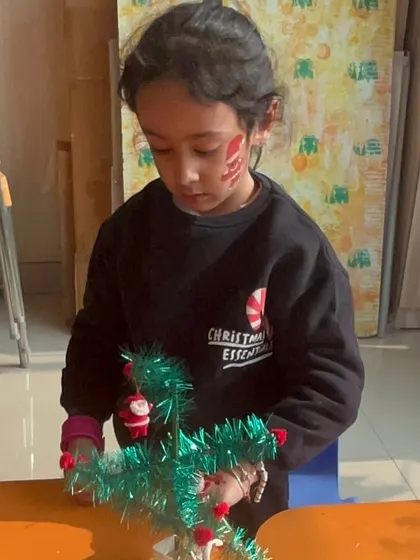 A girl with festive face paint decorates a miniature Christmas tree.