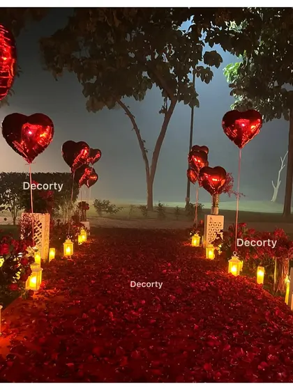 A magical pathway lined with candles in lanterns and red heart-shaped balloons, leading to the proposal spot.
