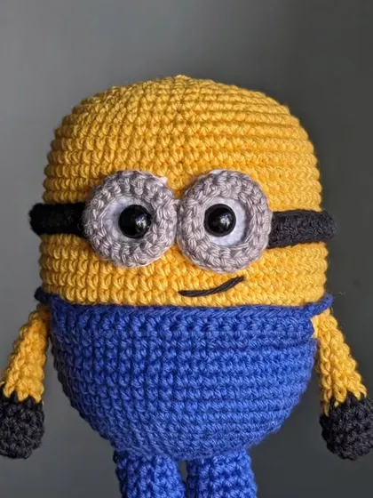 A close-up portrait of the handmade Minion toy, focusing on his large, goggled eyes.