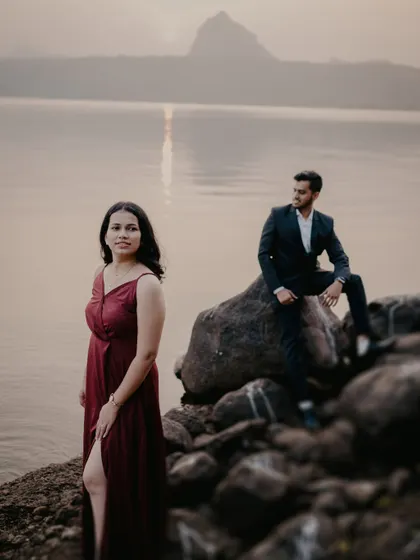 A dramatic, wide-angle shot with the bride in the foreground and the groom perched on a rock behind her. The mountain in the distance adds a majestic feel to this Pune pre-wedding location.