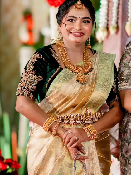 Our client looks stunning in a deep green velvet blouse with exquisite gold floral embroidery. Paired with a golden tissue silk saree and traditional temple jewelry, her look is a perfect blend of richness and grace.