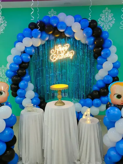 A Boss Baby theme featuring a blue and black balloon ring with a shiny tinsel backdrop. Large foil Boss Baby heads are placed on balloon pillars.