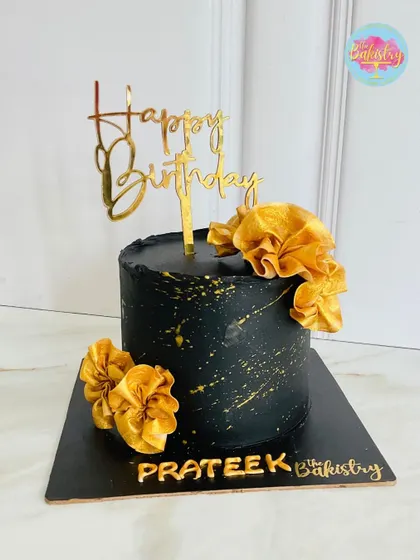 A touch of elegance for a special day. This stunning black and gold cake for Prateek features a dark, moody base with gold splatter and beautiful golden fabric-like flowers.