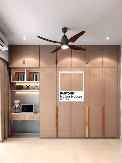 This bedroom showcases a full-wall wardrobe in "Mocha Mousse," Pantone's Color of the Year 2025. The design cleverly integrates a compact study desk and open shelving with backlighting.