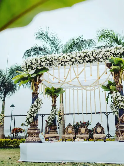 A wide view of the stunning white-themed mandap set against a backdrop of palm trees, perfect for a serene outdoor wedding.