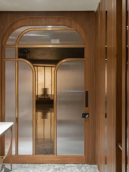 The foyer features an elegant main door with arched, frosted glass panels, offering a grand welcome. A sleek console table and artistic mirror complete the entryway, which is separated from the living area by a slatted wood screen for privacy.