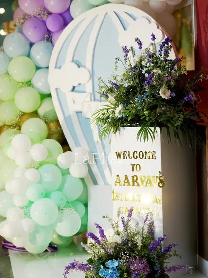 A welcome sign on a pedestal decorated with a hot air balloon cutout and fresh flowers, greeting guests to the carnival.