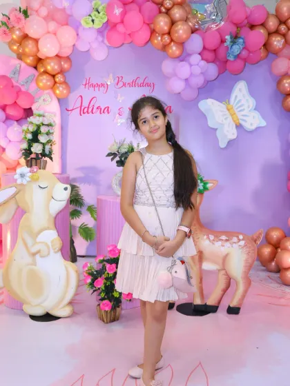 The birthday girl poses at her enchanting woodland-themed party. The large, cute animal props create a storybook setting.