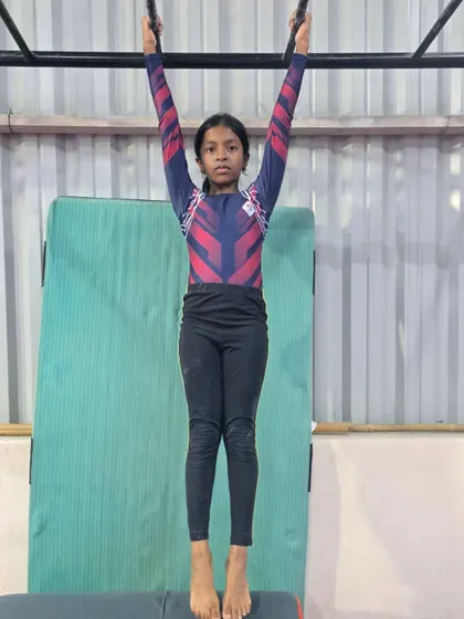 A young gymnast holds a perfect dead hang on the bars, showing excellent posture and strength. This is a fundamental conditioning exercise for all gymnasts.