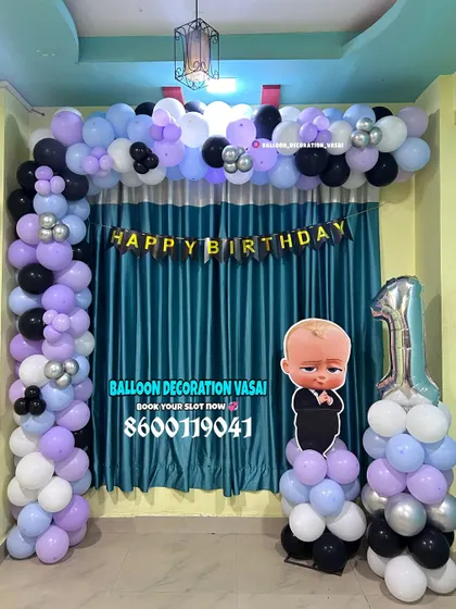 A Boss Baby theme for a first birthday. This simple balloon arch in purple, black, and white is paired with a character cutout and a number '1' foil balloon.