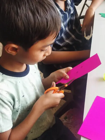 A child practices his scissor skills by carefully cutting colored paper for a craft project.