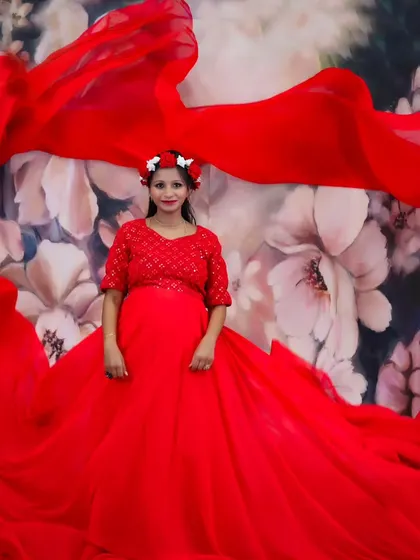 A joyful maternity portrait of a woman in a red gown with a floral headband, surrounded by the flowing red fabric.