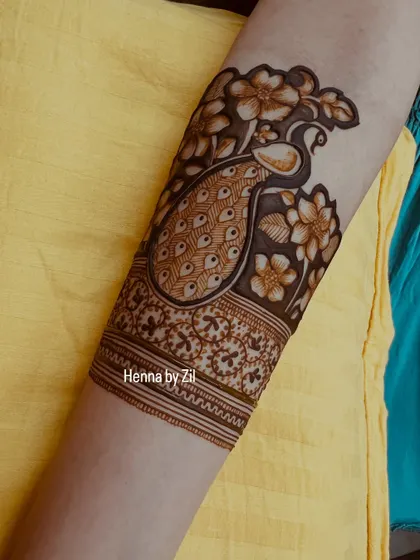 A close-up of an armband featuring a beautiful peacock surrounded by flowers. This shows how the design continues elegantly up the arm.