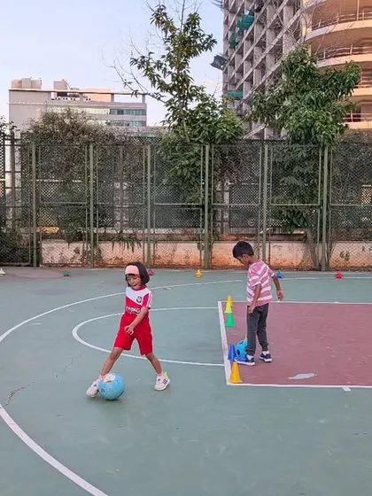Toddlers learning basic football skills on a basketball court, showing our flexibility in using available community spaces.