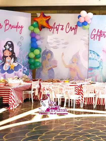 An overview of the activity area, featuring dedicated stations for Hair Braiding, Art & Craft, and Tattoos & Glitter Face Painting, all set against beautifully illustrated mermaid backdrops.