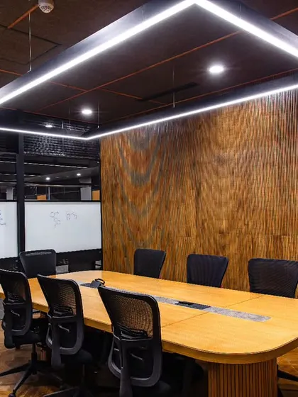 A discussion room at Anthea Pharma designed for functionality and acoustics. The space features wooden paneling, a herringbone-patterned floor, and custom writing boards, all illuminated by a bold, centrally suspended LED fixture.