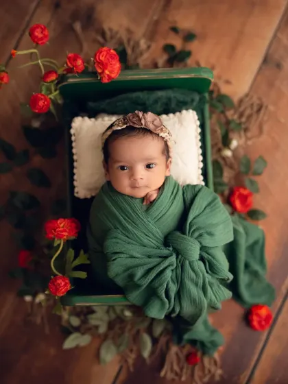 A pop of color with this newborn girl in a green wrap, accented with red flowers. The contrast creates a visually stunning portrait.