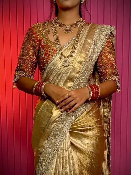 A stunning gold Kanchivaram saree paired with a vibrant red embroidered blouse. The drape is kept classic and clean to showcase the richness of the fabric.