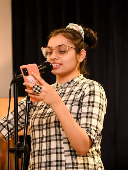 A performer reading from her phone at the microphone. This candid shot captures a real moment during a poetry or storytelling session.