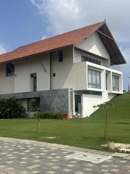 A view of the Vellore International School campus, where buildings with traditional sloping roofs are nestled into green, rolling mounds, reminiscent of a hillside settlement.