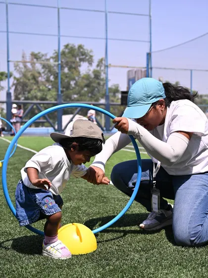 A teacher helps a child crawl through a hoop, part of the toddler obstacle course.
