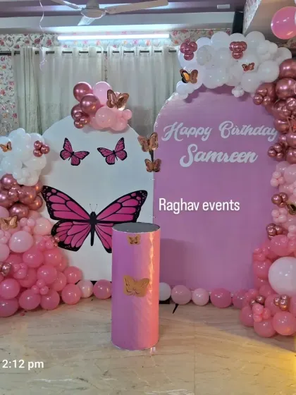 A full view of the pink butterfly themed birthday decoration for Samreen's second birthday. The setup includes backdrops, balloon decorations, and a large light-up number '2'.