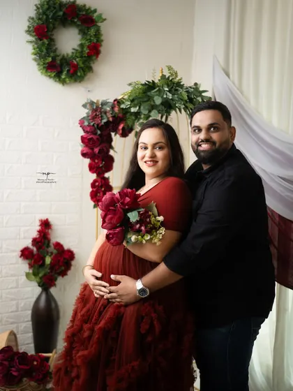 A beautiful portrait of the couple, smiling and ready for their new chapter. The red floral theme adds a touch of romance and glamour to their maternity photos.