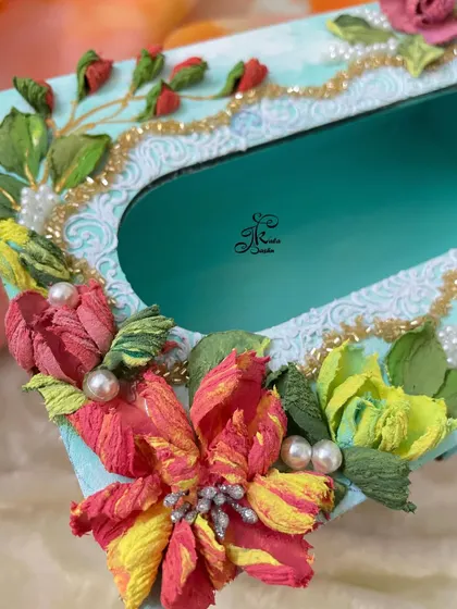 A close-up of a colorful tissue box, showing the intricate details of the multi-colored flowers and pearl accents.