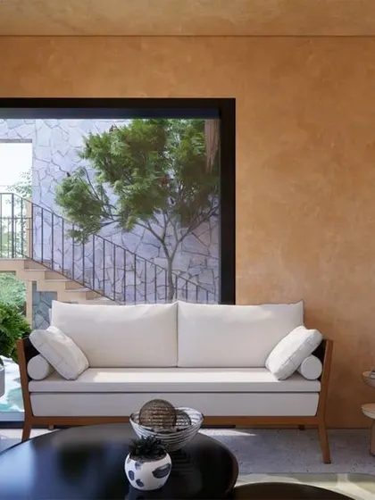 The living room at Earth Abode, with its poured earth walls and large windows, offers a serene view of the pool and the stone-clad exterior staircase.