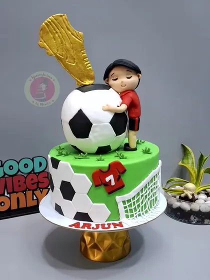 A cake for a young football lover, featuring a golden boot trophy, a large soccer ball, and a custom player figurine.