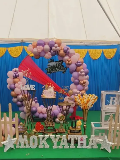 An outdoor tent birthday setup with a beautiful balloon ring in shades of purple, pink, and rose gold.