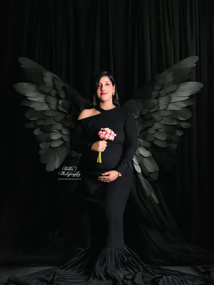 A different take on the black angel wings, this time with the mom-to-be holding a small bouquet, adding a touch of softness to the dramatic studio setup.