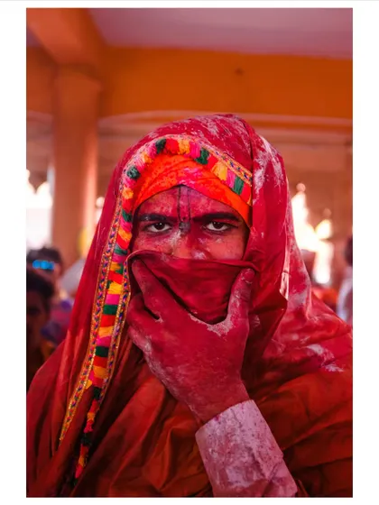 A portrait from the Holi festival, where a man's intense gaze pierces through a veil of vibrant red powder. This image captures the raw, visceral energy of the celebration.