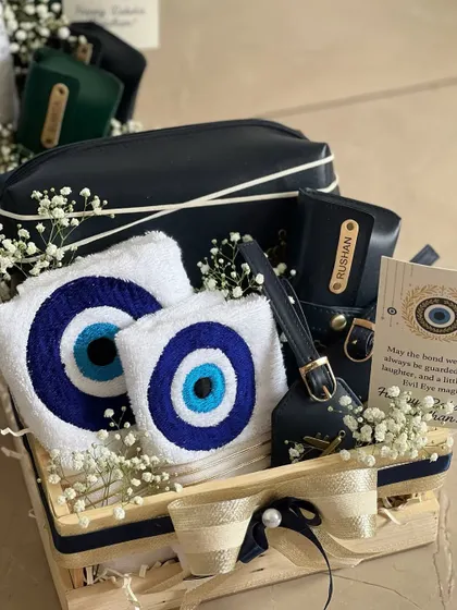 A close-up of the Evil Eye Rakhi Hamper. You can see the personalized luggage tag, the embroidered towels, and the custom card, all beautifully arranged with baby's breath.
