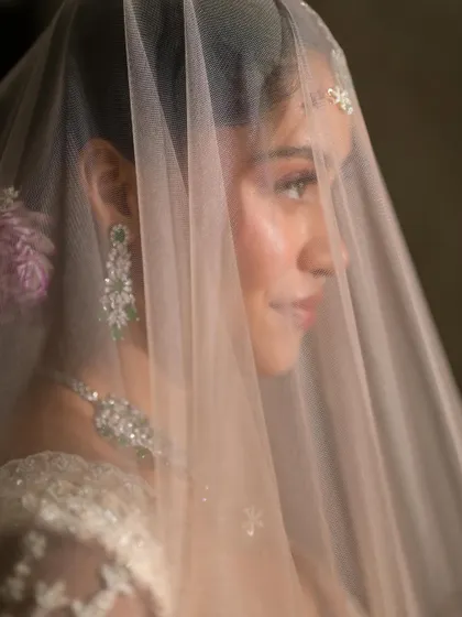 An ethereal bridal look captured through a delicate veil. The makeup is subtle, clean, and natural, with a focus on a magical glow.