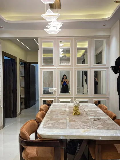 Another view of the dining area, showing how the mirrored wall reflects the entire room, including the modern chandelier, making the space feel grand.