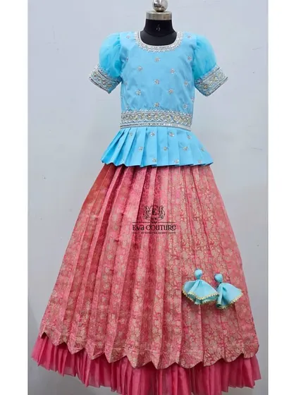 A similar design in a sky blue and pink combination. The blue peplum top is paired with a pink Banarasi skirt with a double-layered, scalloped hem.