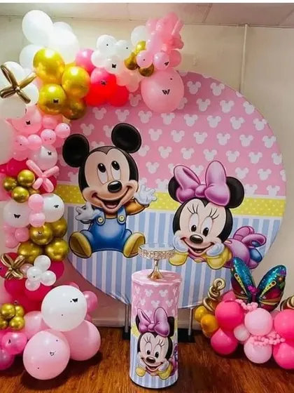 A cute Mickey and Minnie Mouse themed setup. This decoration features a character backdrop, a pink and gold balloon arch, and a themed pedestal.