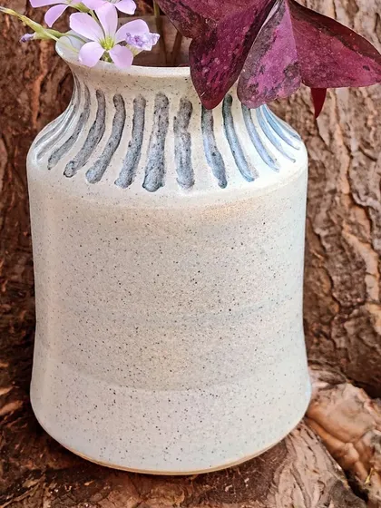 This stoneware vase features hand-carved vertical lines that add a simple, elegant texture. It's designed to hold a few fresh stems from the garden, bringing a touch of nature indoors.