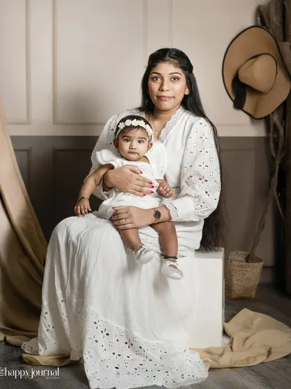 An elegant studio portrait of a mother and baby, with the father's presence implied by his hat in the background. A creative take on a family photo.