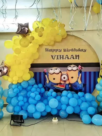A Minions-themed birthday party. This setup includes a character backdrop and a blue and yellow balloon arch with Minion foil balloons.