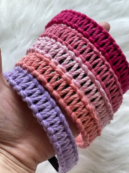 Holding a selection of my handmade macrame hairbands to show their texture and vibrant colors. This stack includes shades of lavender, peach, and multiple tones of pink, highlighting the detailed knotwork.
