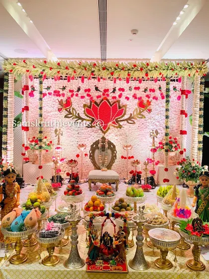 A wide-angle shot of the puberty ceremony decoration. The symmetrical arrangement of offering plates, dolls, and floral elements creates a balanced and visually stunning scene.