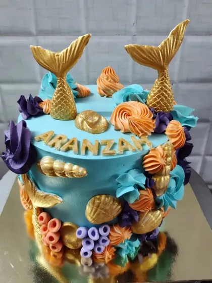 An enchanting mermaid-themed cake perfect for a magical birthday. This custom cake is decorated with golden mermaid tails, colorful buttercream corals, and delicate seashells.