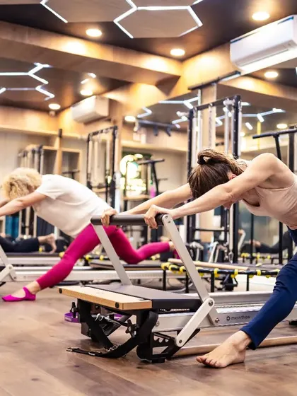 A beautiful shot of a group performing a deep lunge stretch on the Reformers. This highlights the focus on flexibility and creating long, lean lines in the body.