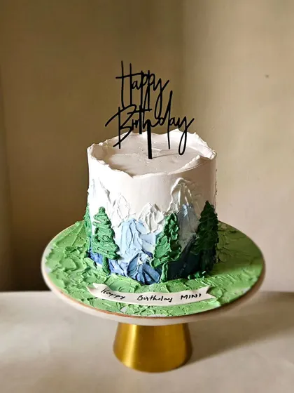 I used a palette knife and whipped cream to paint this mountain scene directly onto the cake. The textured peaks and trees create a rugged, natural landscape, perfect for someone who loves the outdoors.